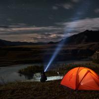 Man using flashlight in campsite at night